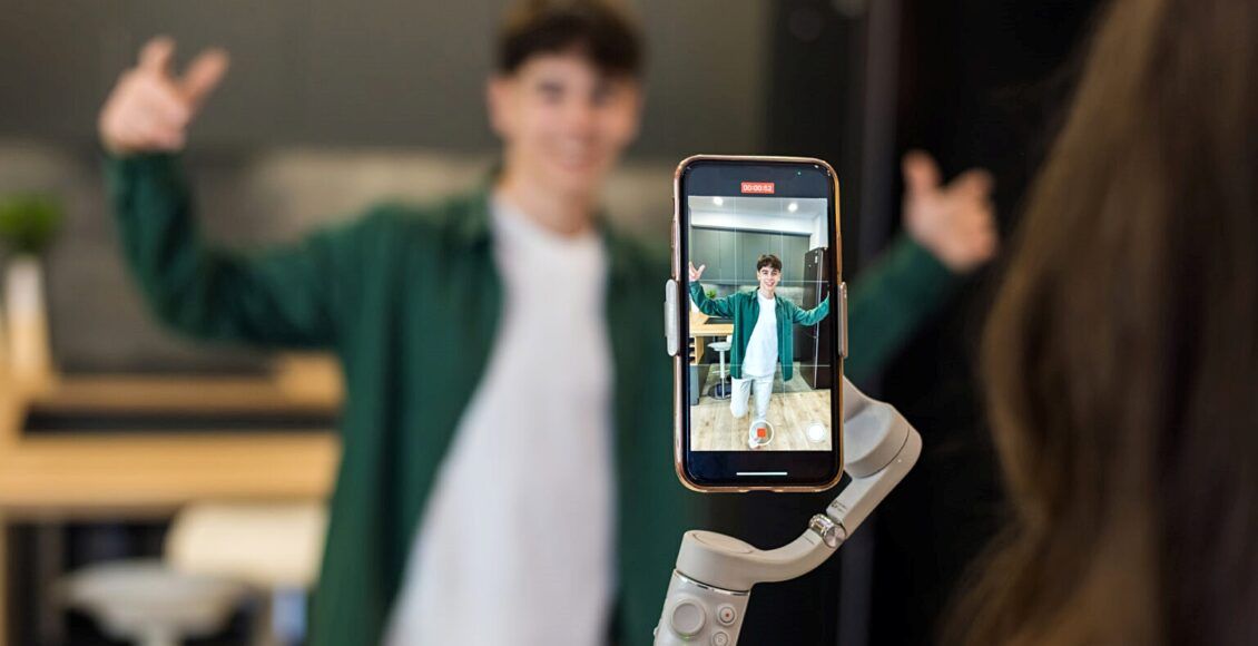 A person recording a young dancing man blogger influencer on smartphone on a stabiliser in a studio